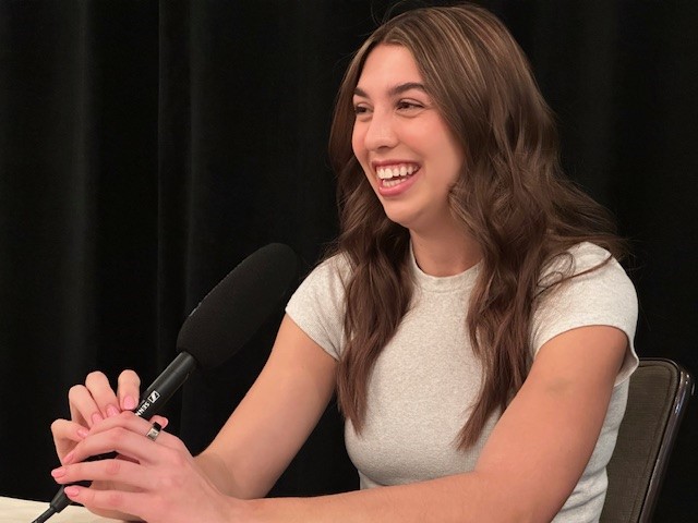 A woman smiles while sitting at a microphone