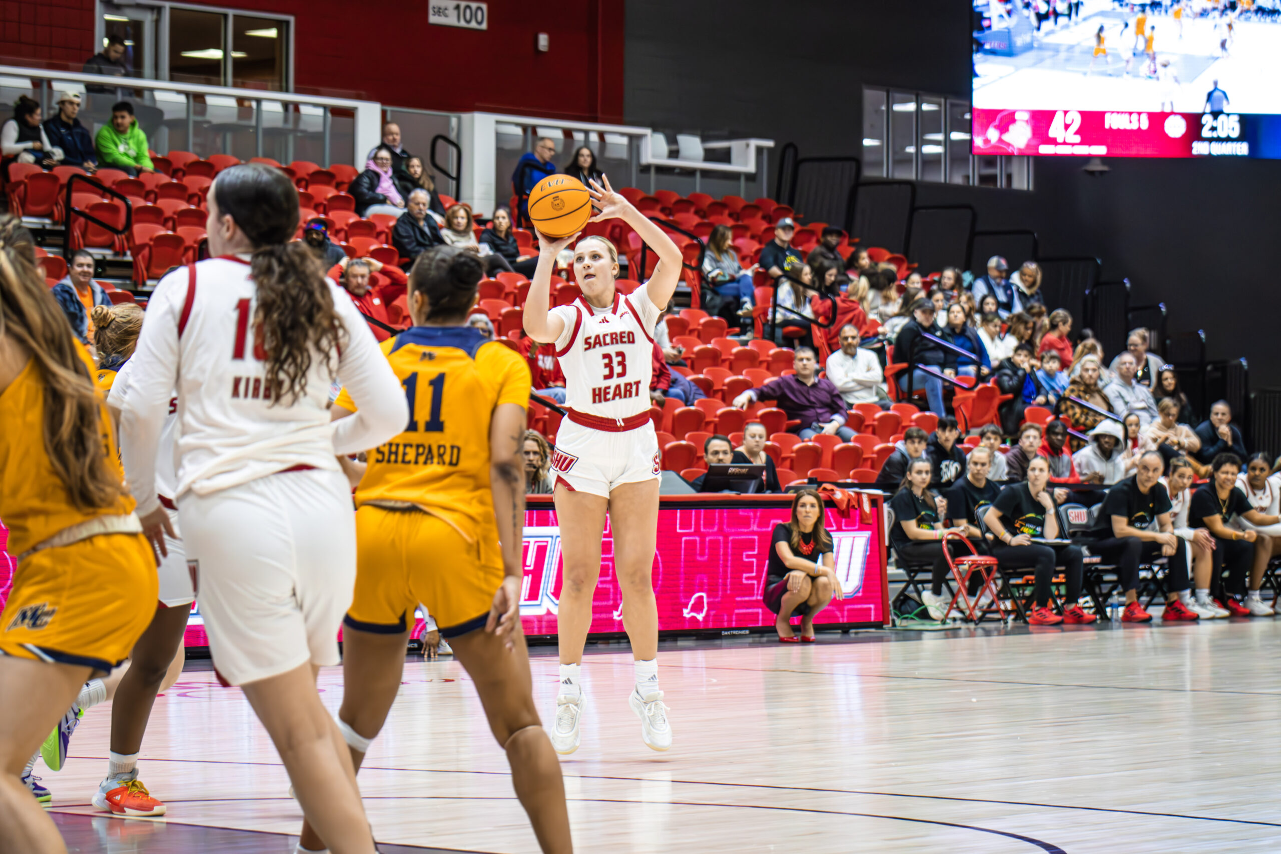 Sacred Heart junior guard No. 33 Amelia Wood (in white, high in the picture) looks toward the basket and shoots a three in the Pioneers 74-48 win over Merrimack on Thursday, Feb. 20.