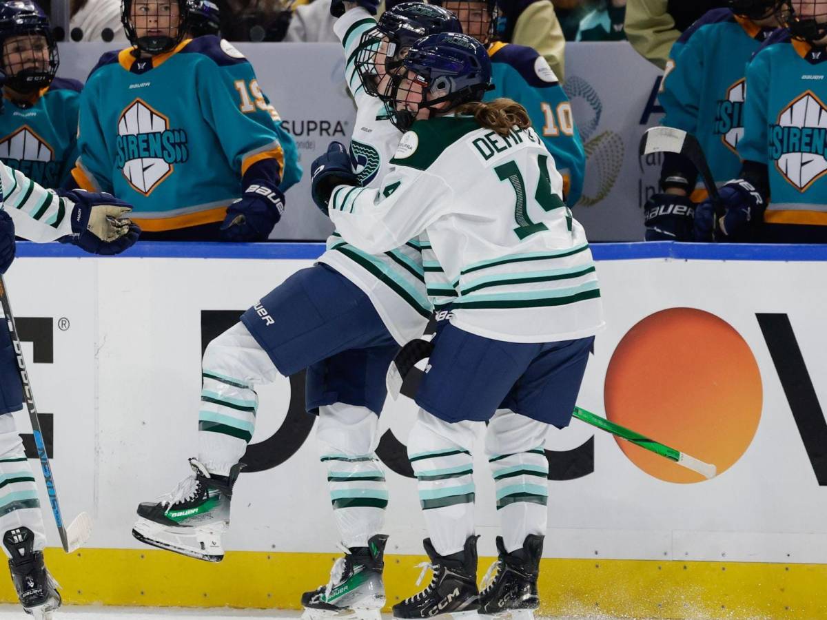 Gabel raises her arm in celebration as Dempsey hugs her from behind. They are wearing white away uniforms.