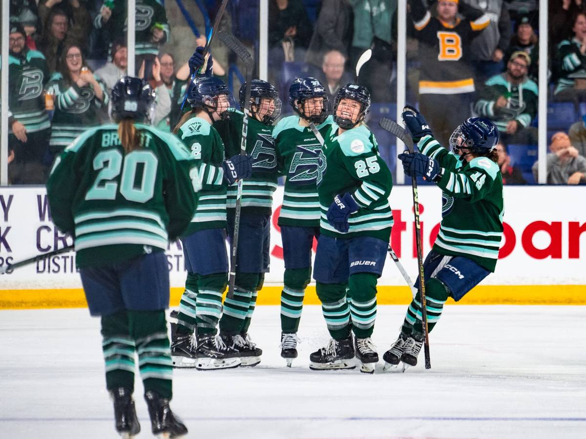 Five Boston Fleet players celebrate with a group hug. Hannah Brandt is skating to join. They are wearing green home uniforms.