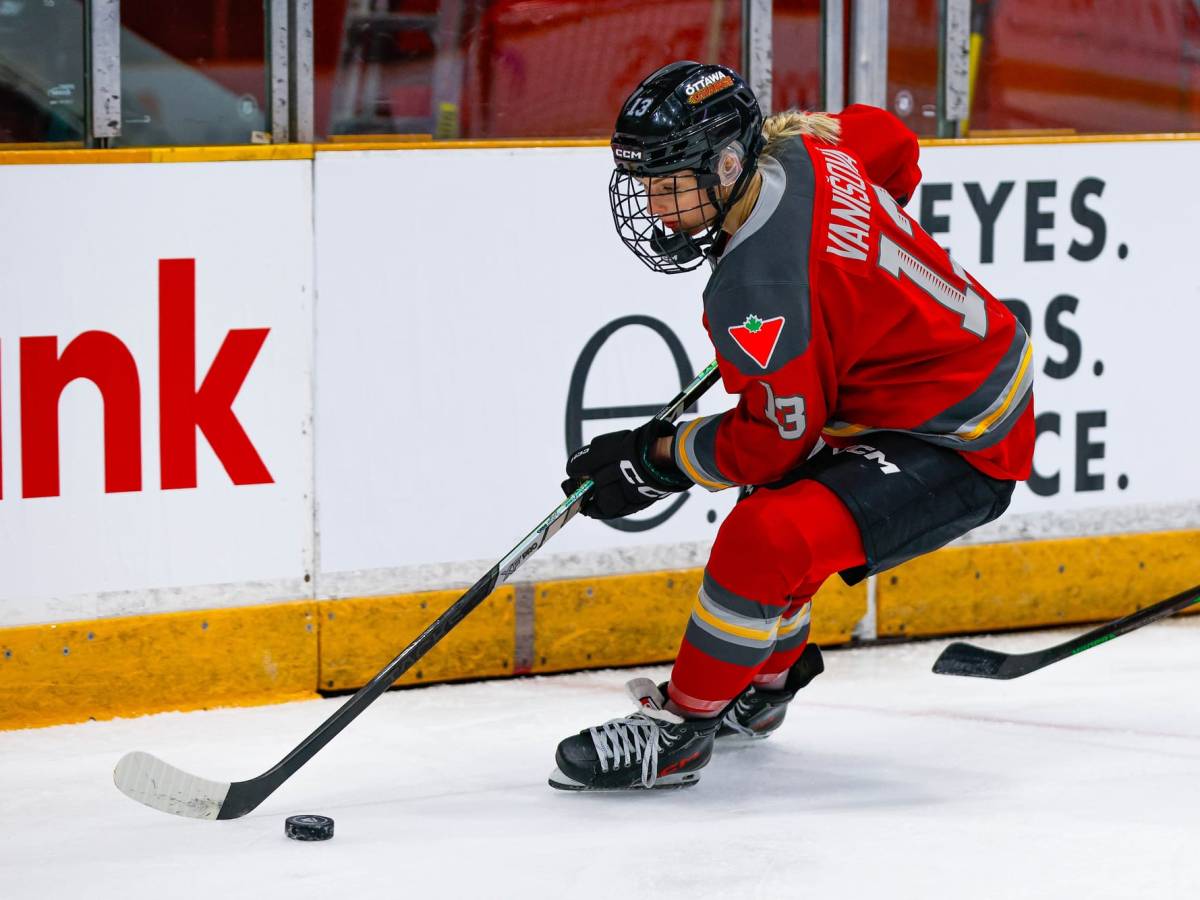 Vanišová looks down at the puck as she skates along the boards. She is wearing a red home uniform.