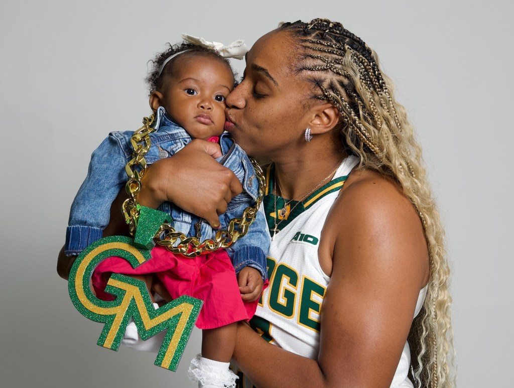 George Mason forward Nalani Kaysia holds up her daughter Xéla and kisses her cheek. Xéla is wearing a GM (George Mason logo) necklace.