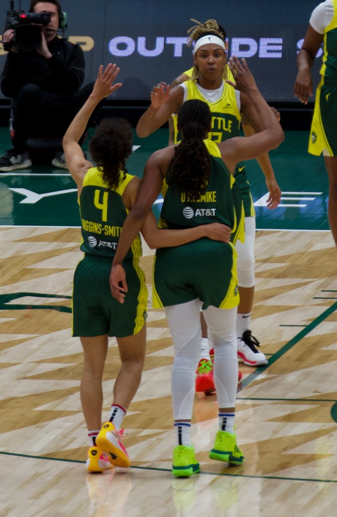 Seattle Storm guard Skylar Diggins-Smith wraps her right arm around Nneka Ogwumike. Both of them raise one hand to high-five teammate Jordan Horston.