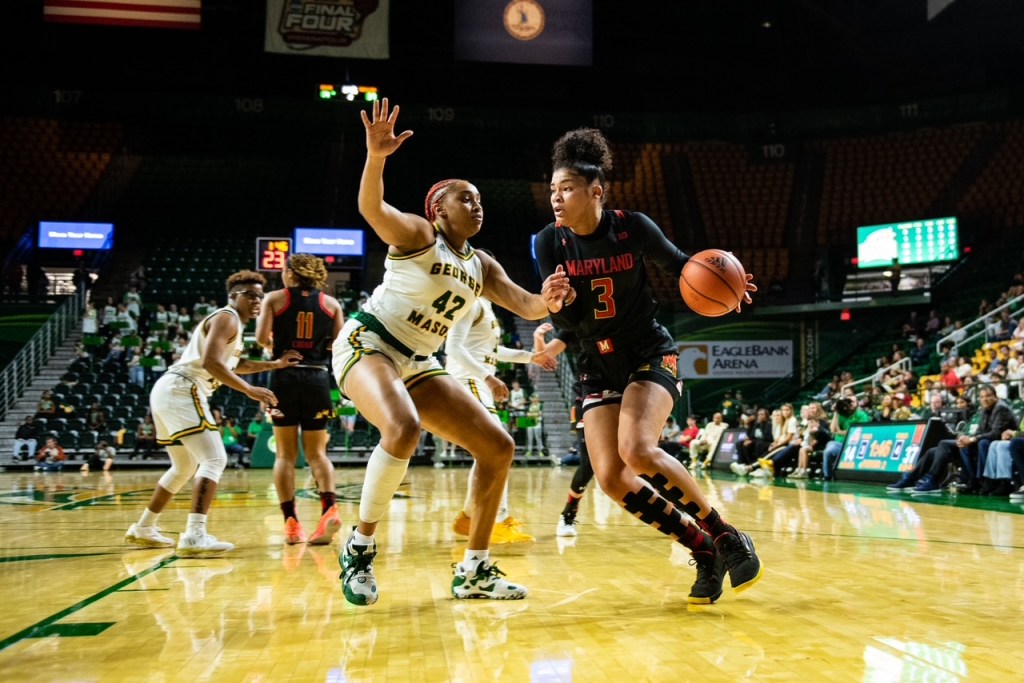 George Mason forward Nalani Kaysia defends with her left foot planted on the ground and her arms outstretched as an opposing player drives toward the basket.