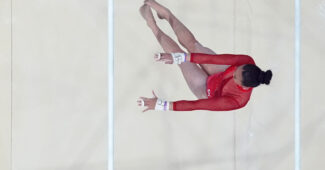 A gymnast in a red leotard competing on the uneven bars over a white mat.