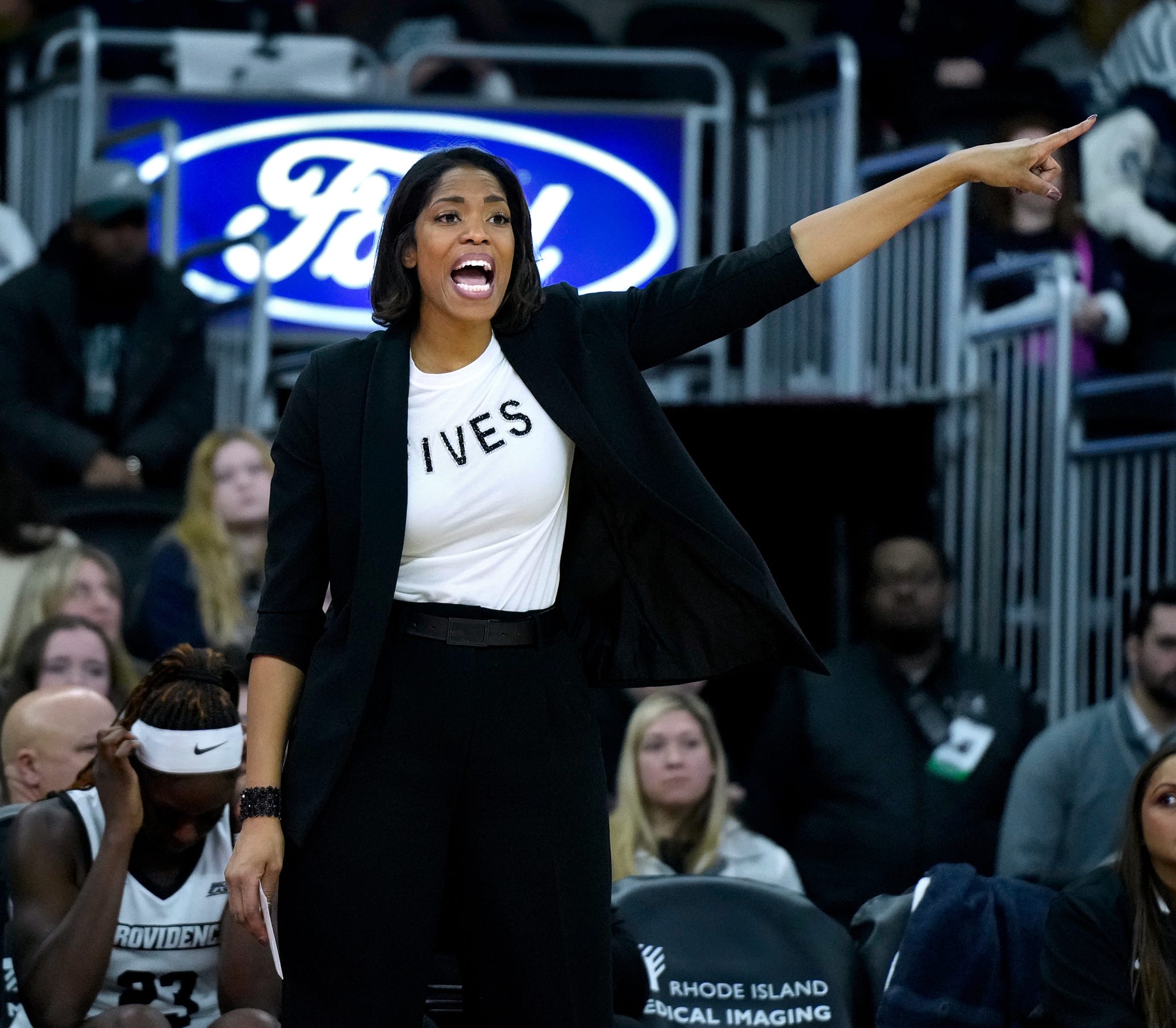 Providence head coach Erin Batth extends her left arm out to the side as she signals to her team from the sideline.