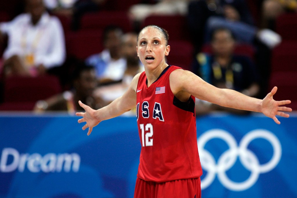 Diana Taurasi stands in a USA jersey with both arms outstretched to the side