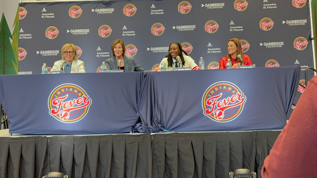 Amber Cox, Kelly Krauskopf, Natasha Howard, and Stephanie White of the Indiana Fever sit at a table on a podium for a press conference.