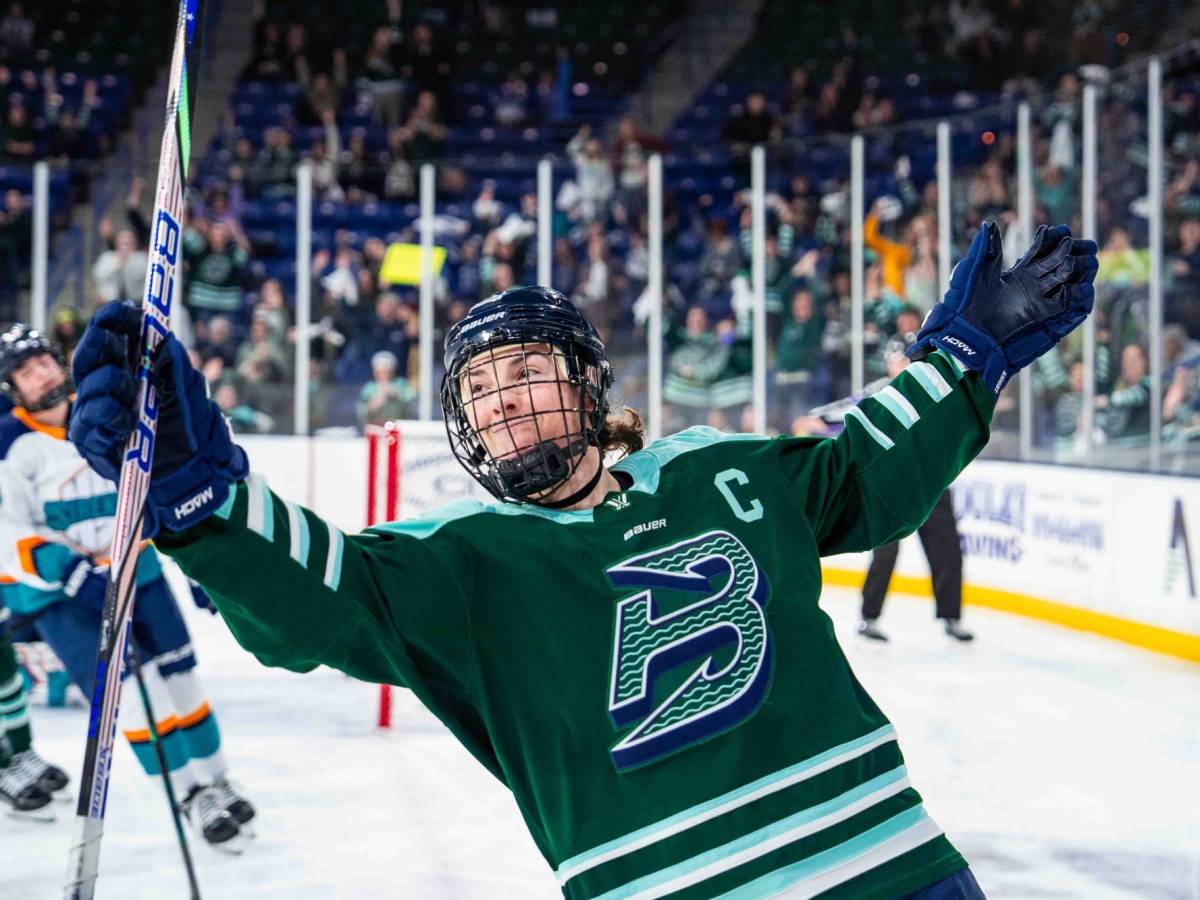 Knight raises her arms and smiles as she skates away from the net. She is wearing a green home uniform.