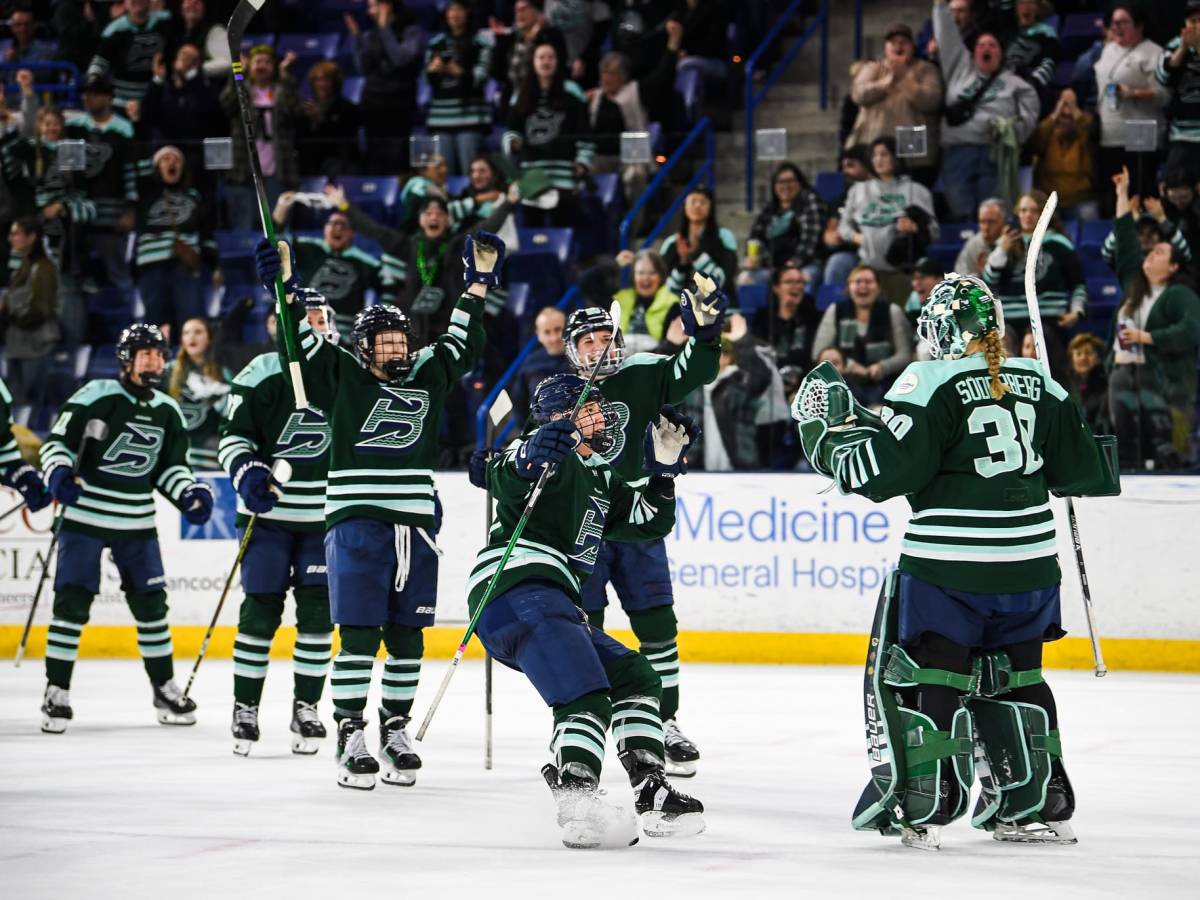 Fleet players smile and skate toward Söderberg, who is pumping her fists. They are wearing green home uniforms.