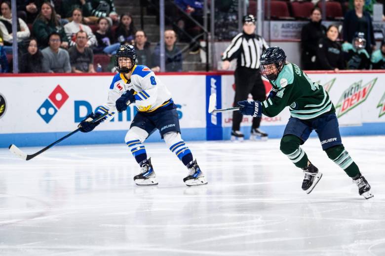 Saulnier (right in green) skates hard at the puck, as Flanagan (left in white) also pursues the puck.