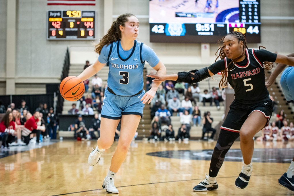 Columbia guard Cecelia Collins dribbles the ball with her right hand on the perimeter. She has her eyes up, looking across the court, as Harvard guard Gabby Anderson slides her feet to defend her.