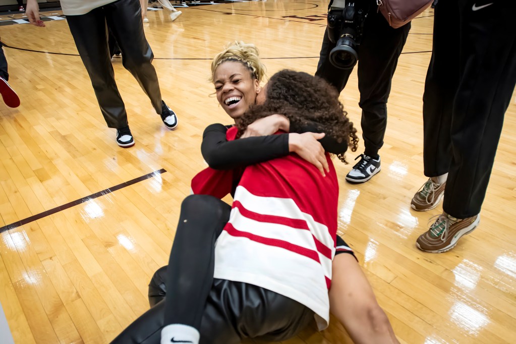 Harvard guard Harmoni Turner lies on the floor and hugs head coach Carrie Moore. Moore is hugging her back and has her head buried in Turner's shoulder.