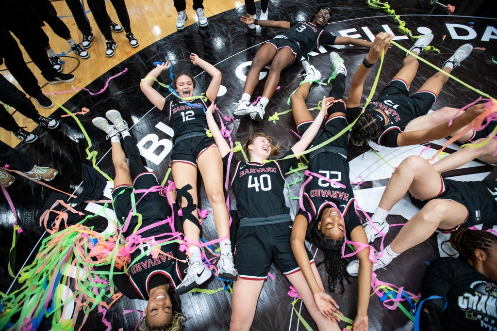 Harvard players lay on the center court logo after winning the Ivy League Tournament and bask in rainbow streamers strewn across the court.