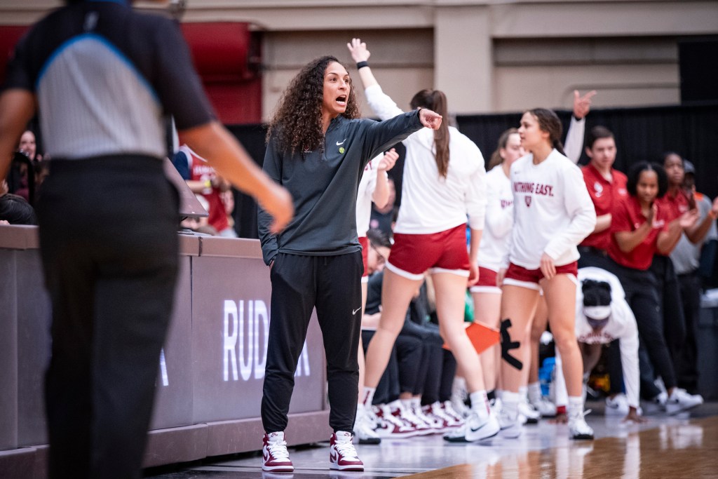 Harvard head coach Carrie Moore stands on the sideline in front of the scorer's table. She points to something on the court with her left hand and shouts instructions.