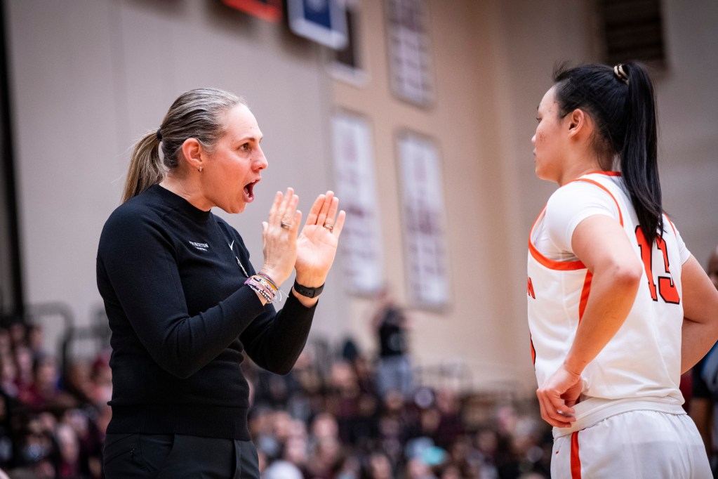Princeton head coach Carla Berube talks to point guard Ashley Chea during a game. Berube has her hands at about chest height and close together, with her palms facing one another, as she talks.