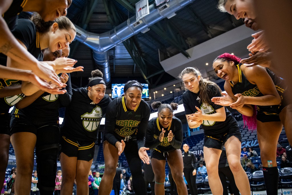George Mason players clap their hands and cheer while standing in a circle before a game.