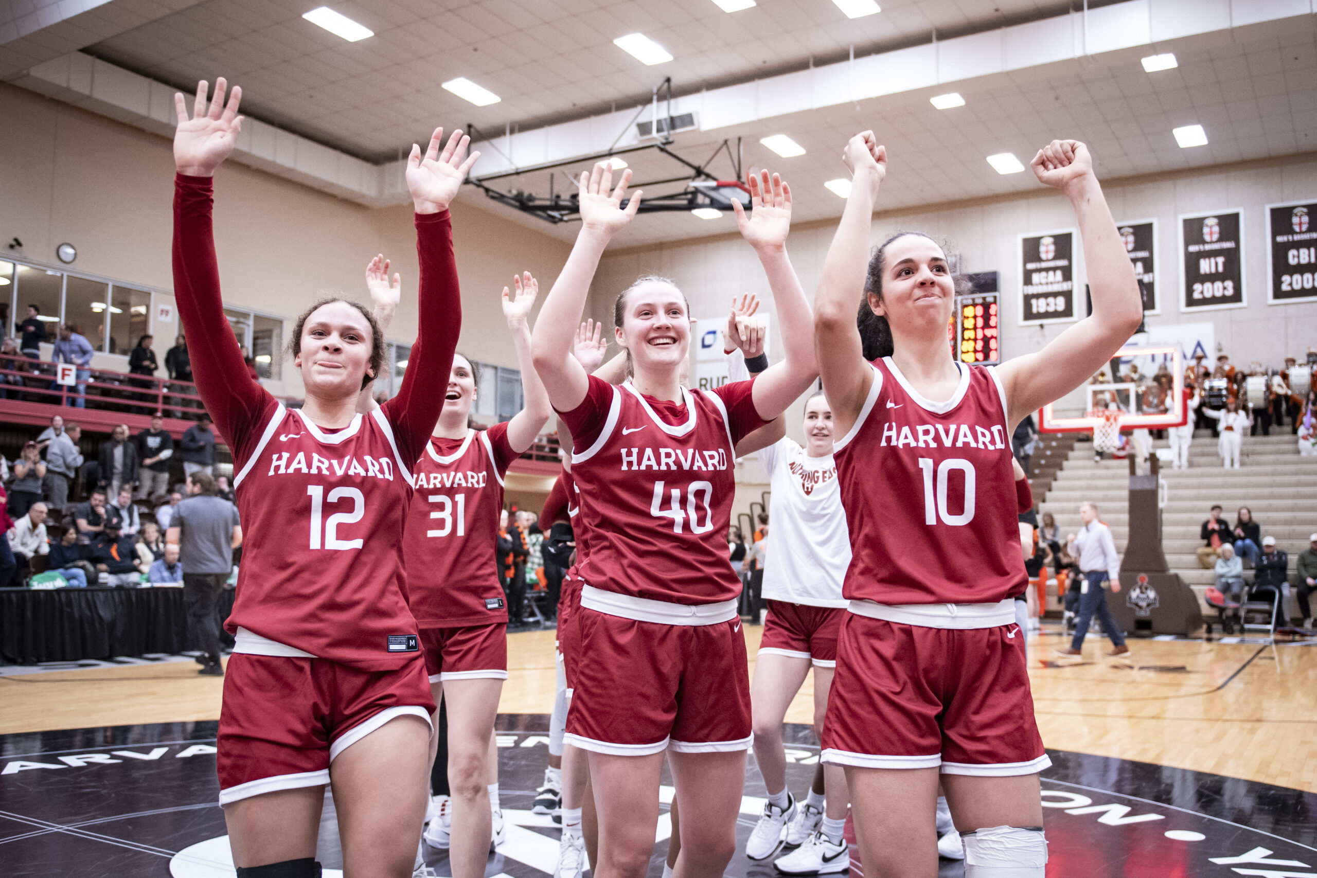 Several Harvard players stand at halfcourt and wave with both hands toward their supporters section after a game.