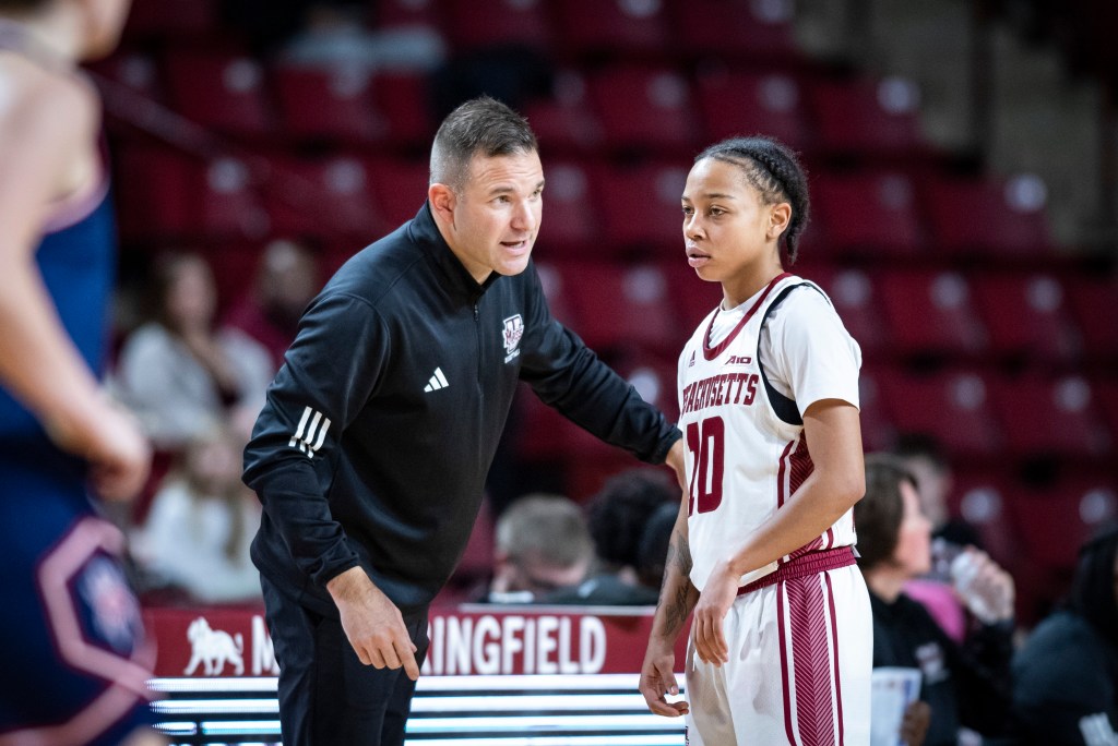 UMass head coach Mike Leflar leans over to talk to UMass freshman guard Yahmani McKayle, who listens intently while looking down the court.