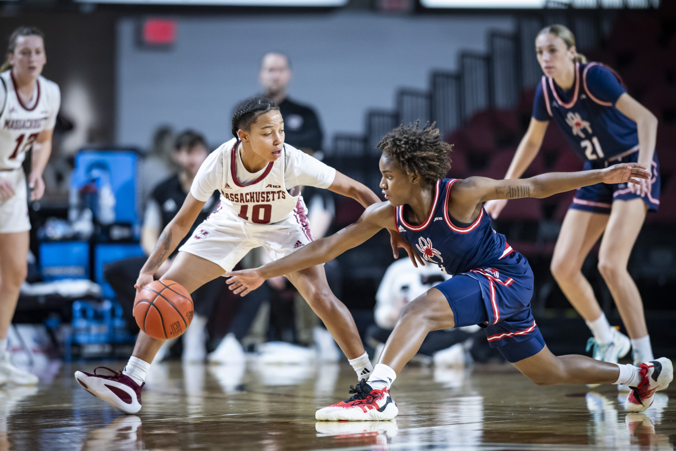 UMass freshman guard Yahmani McKayle corrals the ball with her right fingertips with her legs in a wide stance as a defender tries to get a steal. The defender has her arms outstretched and legs in a lunge position.