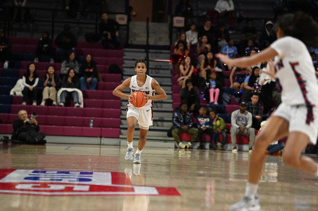 Penn guard Mataya Gayle holds the ball with two hands, ready to make a chest pass to a teammate cutting up the court.