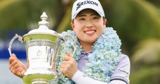Rio Takeda, wearing a flowered boa, holds the Blue Bay LPGA trophy to her right side and smiles.