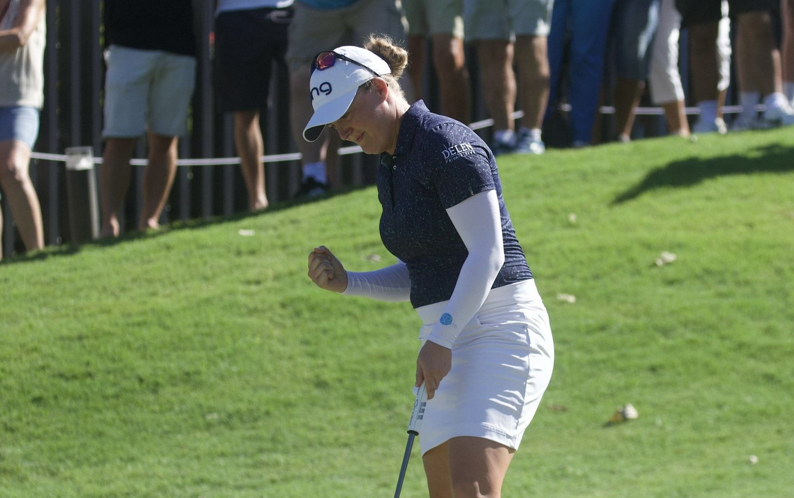 Manon De Roey moves toward the hole with her putter in her hand and her other hand in a fist, celebrating.