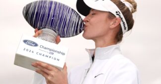 Nelly Korda holds up a trophy to her right side and kisses the side of it to celebrate a victory.