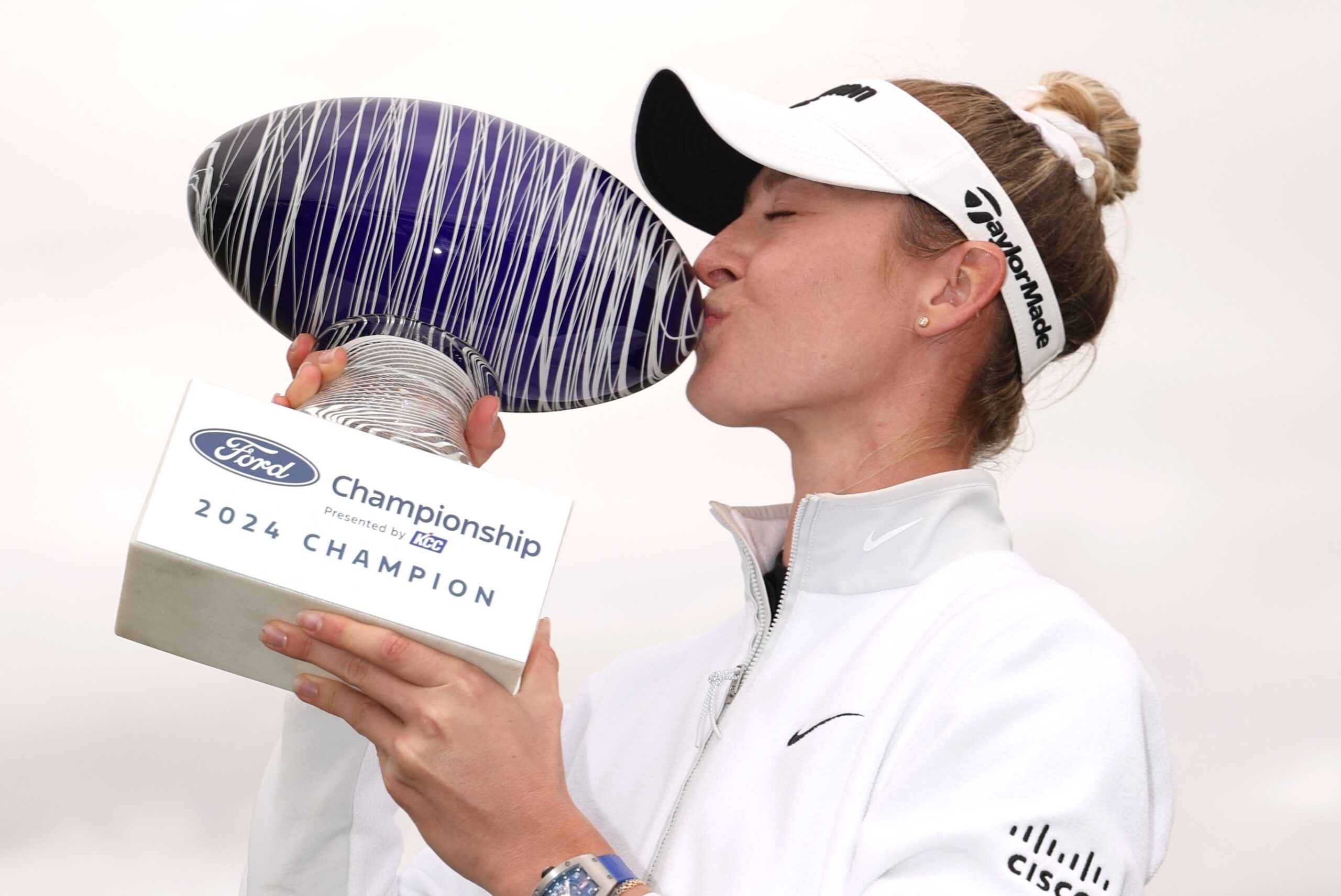 Nelly Korda holds up a trophy to her right side and kisses the side of it to celebrate a victory.