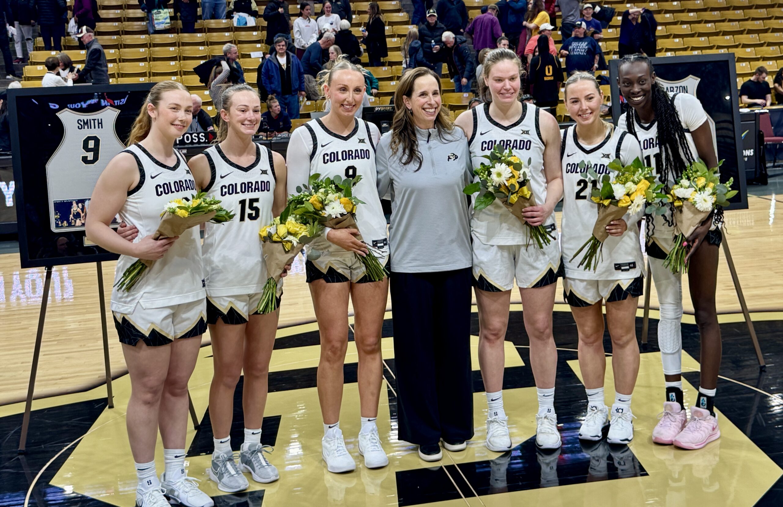 Six Colorado basketball players stand at center court with the head coach of the team.