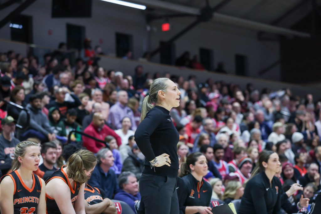 Princeton head coach Carla Berube stands on the sideline with her hands on her hips, looking out at the on-court action.