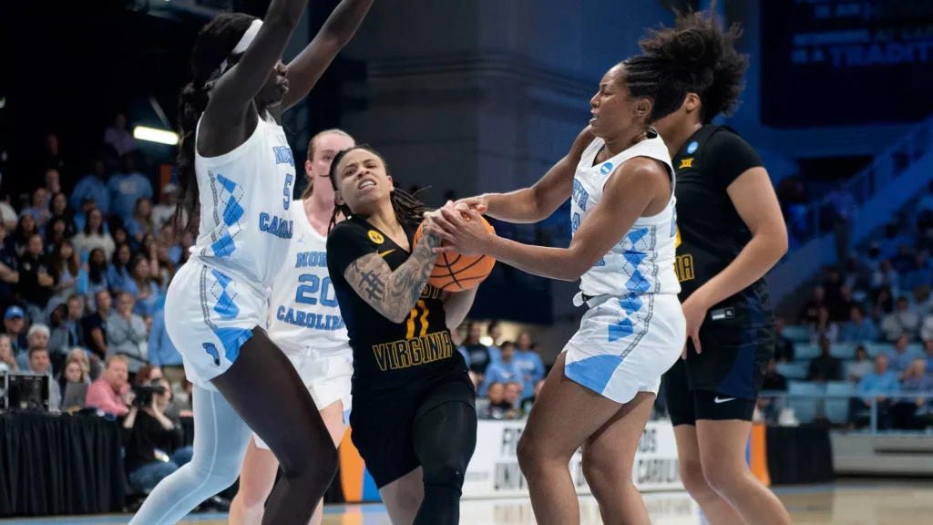 North Carolina guard Indya Nivar gets her hands on the ball as JJ Quinerly holds it tightly with both hands, trying to turn away and drive to the basket. Maria Gakdeng is positioned directly behind Quinerly with extended arms, preventing her from moving away from Nivar.