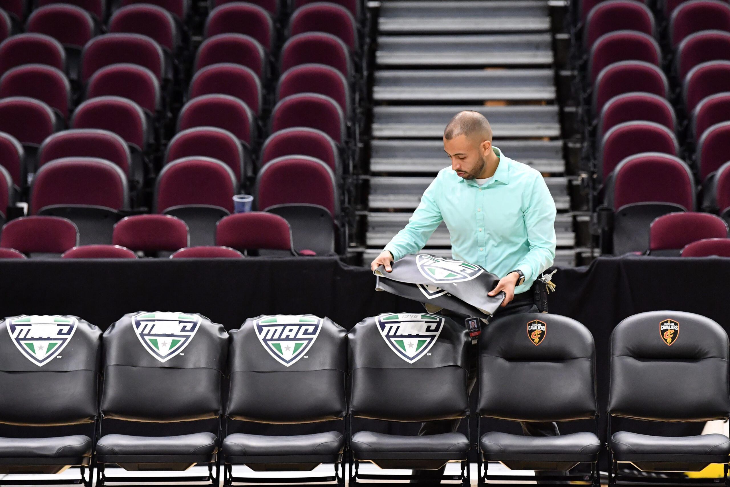 A worker removes the insignia of the Mid-American Conference from the bench chairs at Rocket Mortgage FieldHouse after the 2020 Mac Tournament was cancelled. (Photo Credit: Ken Blaze | USA TODAY Sports)