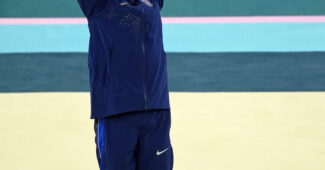 A gymnast in a blue warm up suit cheers.