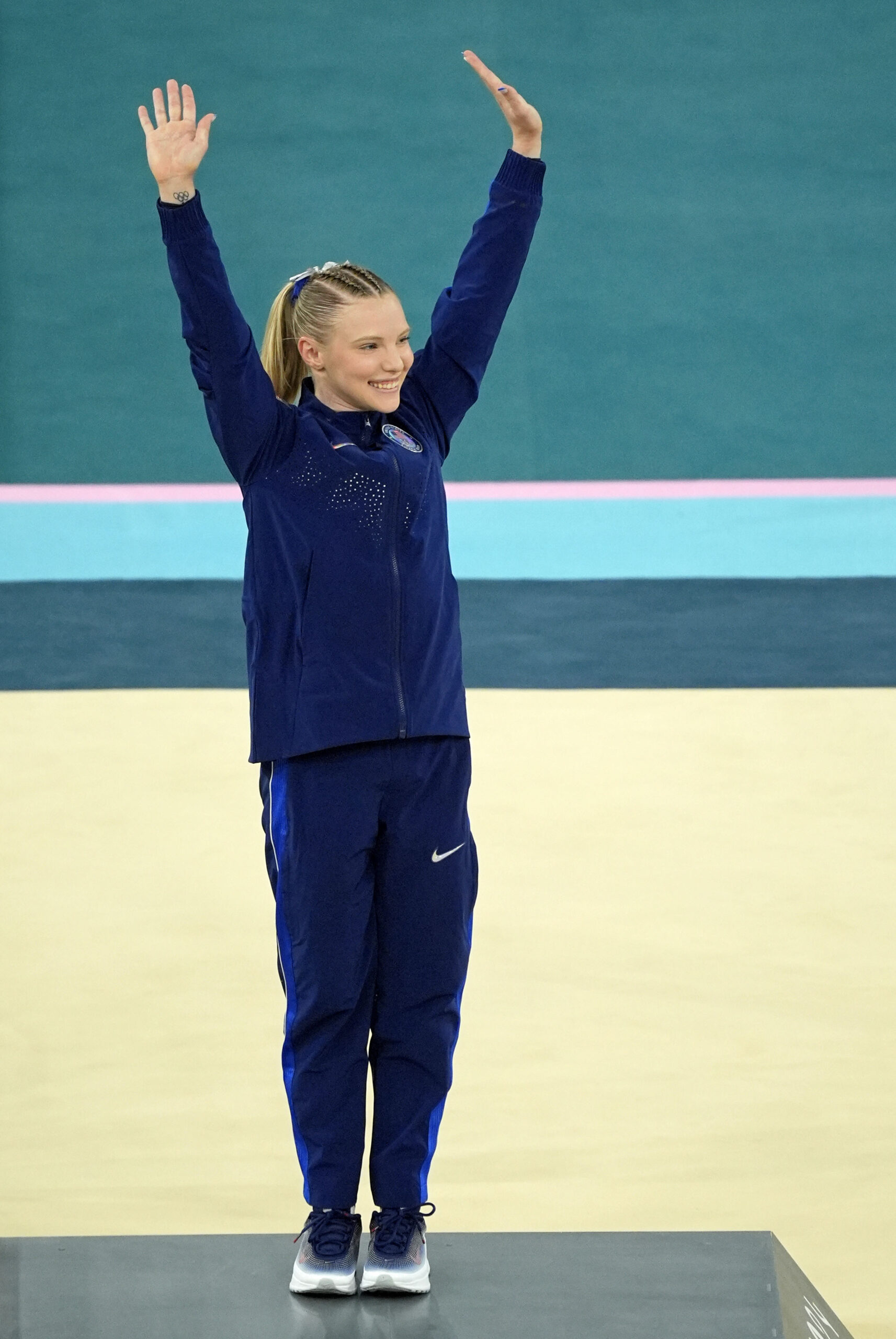A gymnast in a blue warm up suit cheers.