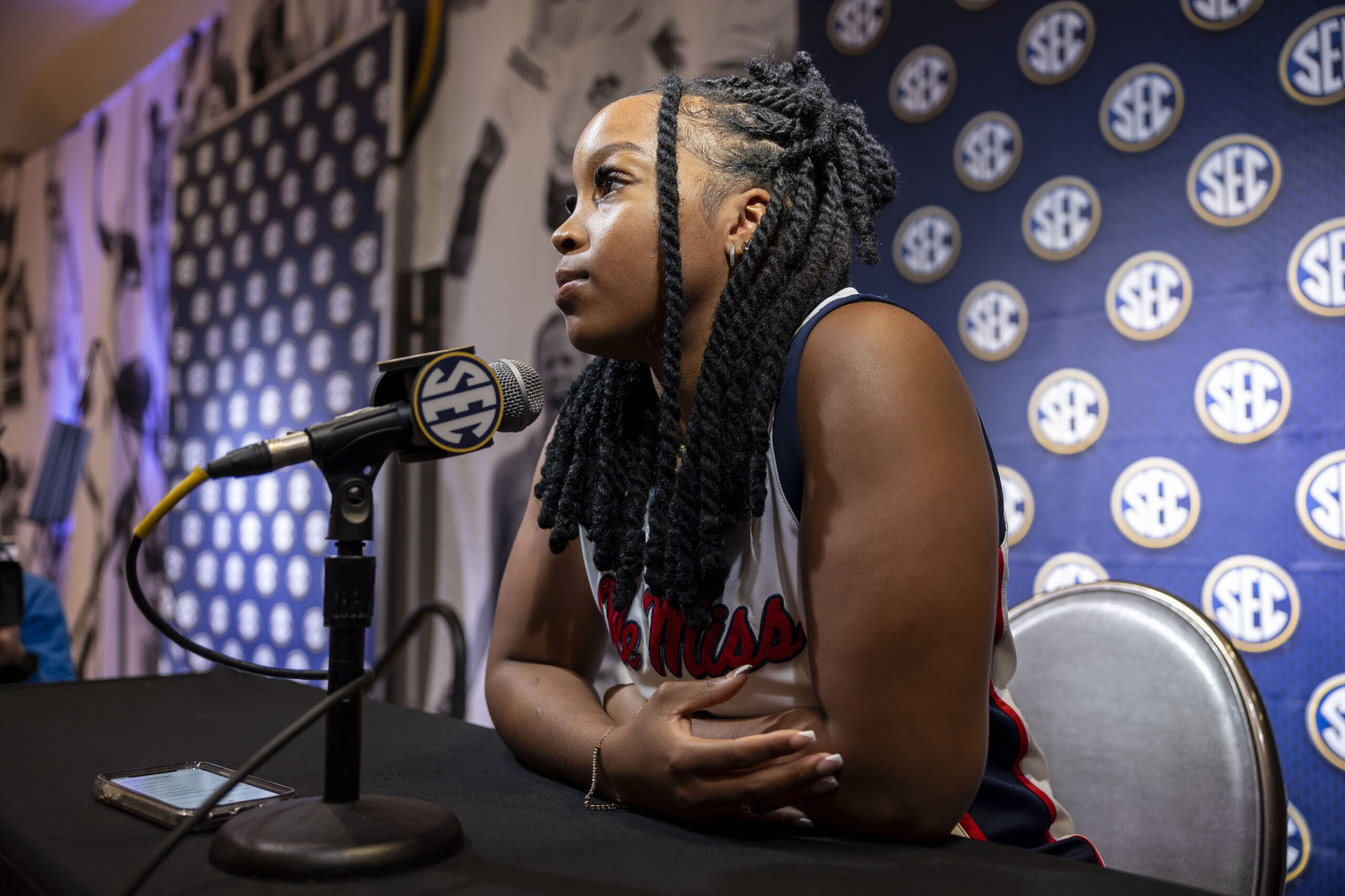 Mississippi guard KK Deans sits at a podium with her arms crossed on the table in front of her. A microphone with the SEC logo is directly in front of her, and she looks out at the assembled reporters.