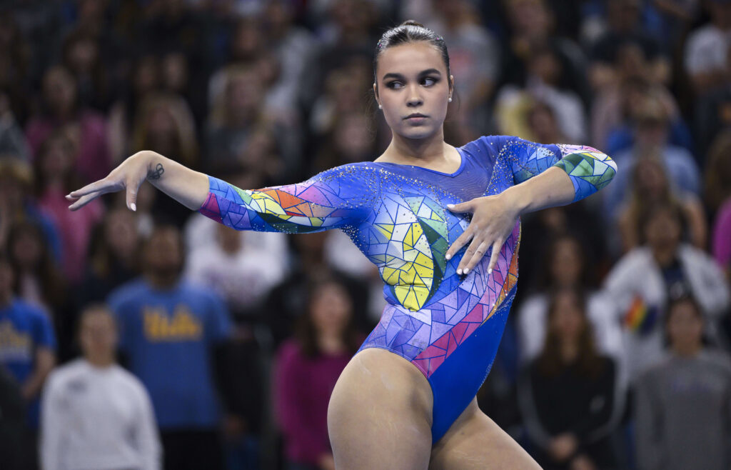 A gymnast in a multicolored leotard does a pose on the floor.