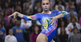 A gymnast in a multicolored leotard does a pose on the floor.
