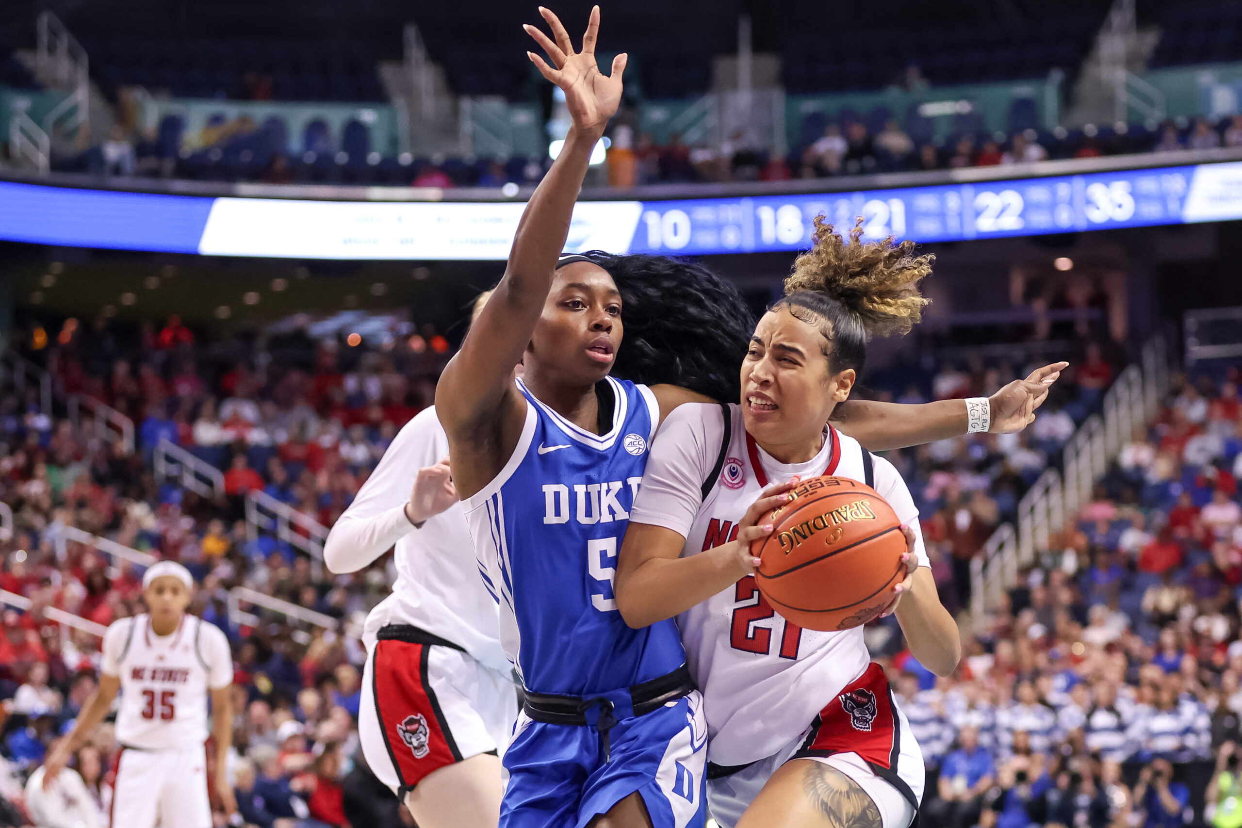 NC State Wolfpack guard Madison Hayes holds the ball with both hands, away from the outstretched arms of Duke Blue Devils guard Oluchi Okananwa standing closely beside her