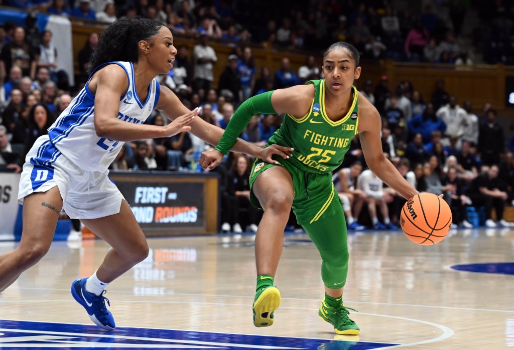 Oregon guard Deja Kelly is mid-step handling the ball in her left hand, while extending her right arm to prevent Duke guard Reigan Richardson from moving in.