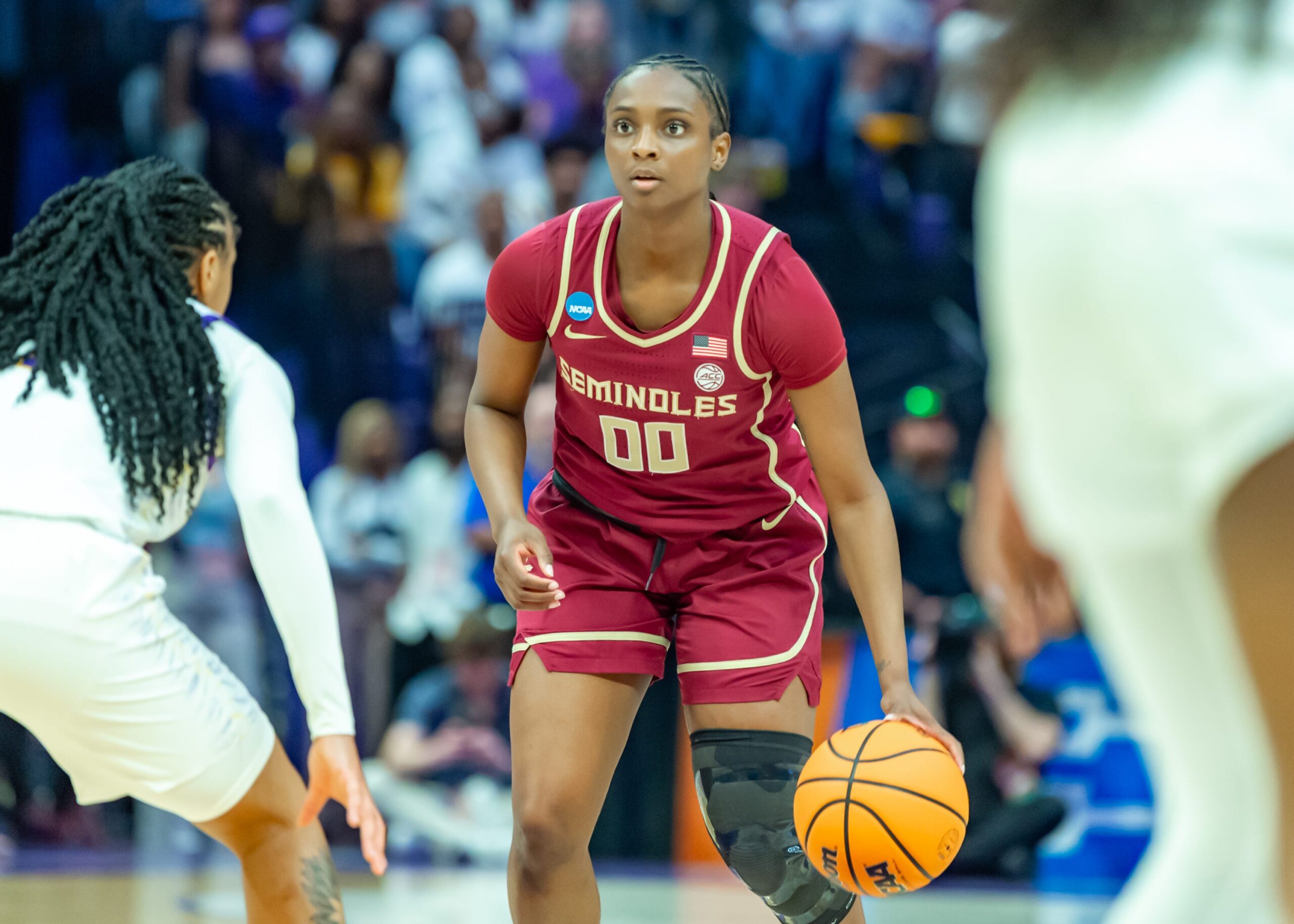 Florida State junior guard Ta’Niya Latson looks down the court as a defender stands ready in front of her and slightly to the right. Latson stands, dribbling the ball with her left hand