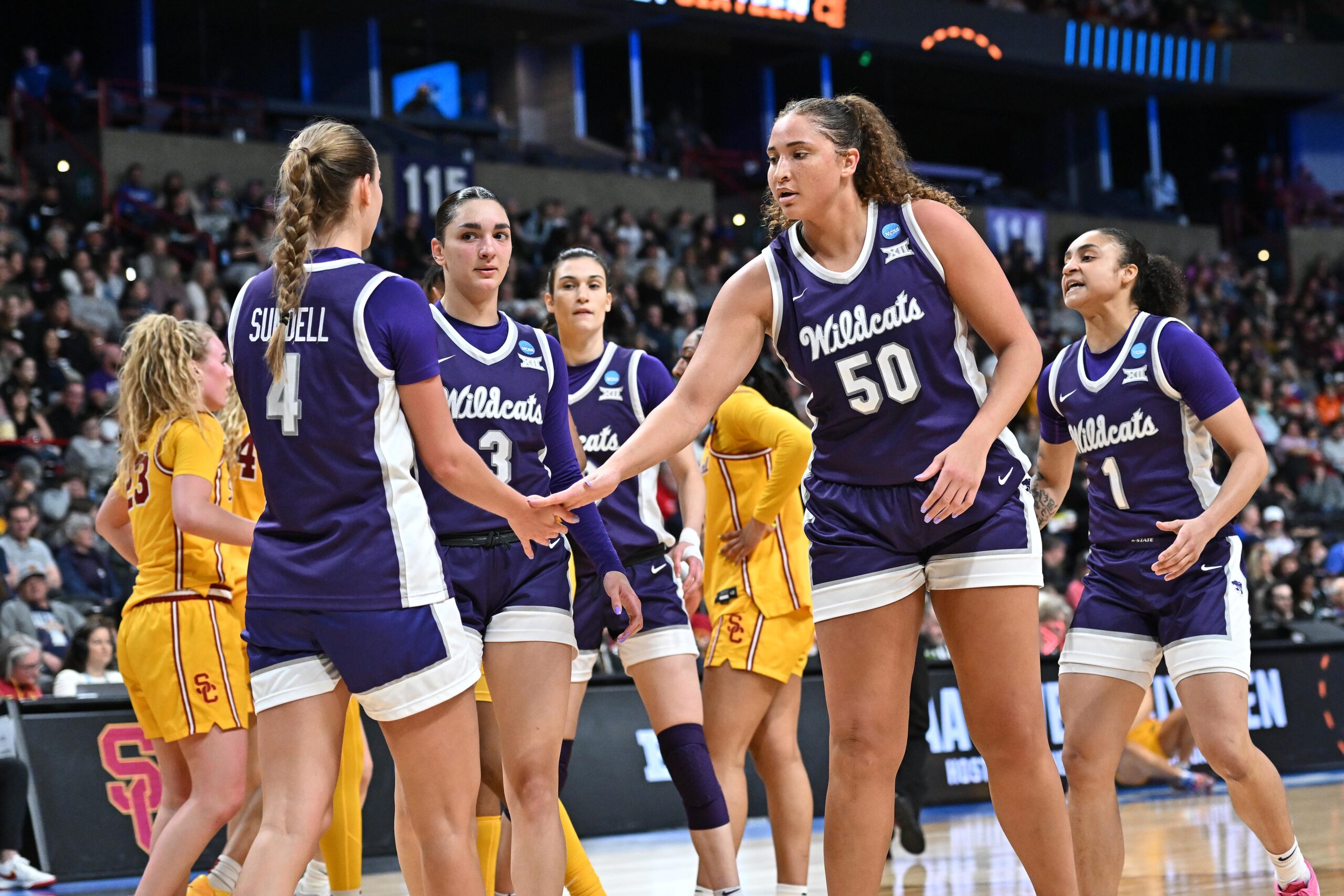 Kansas State players high five during a huddle in a game against USC. USC players stand behind them.