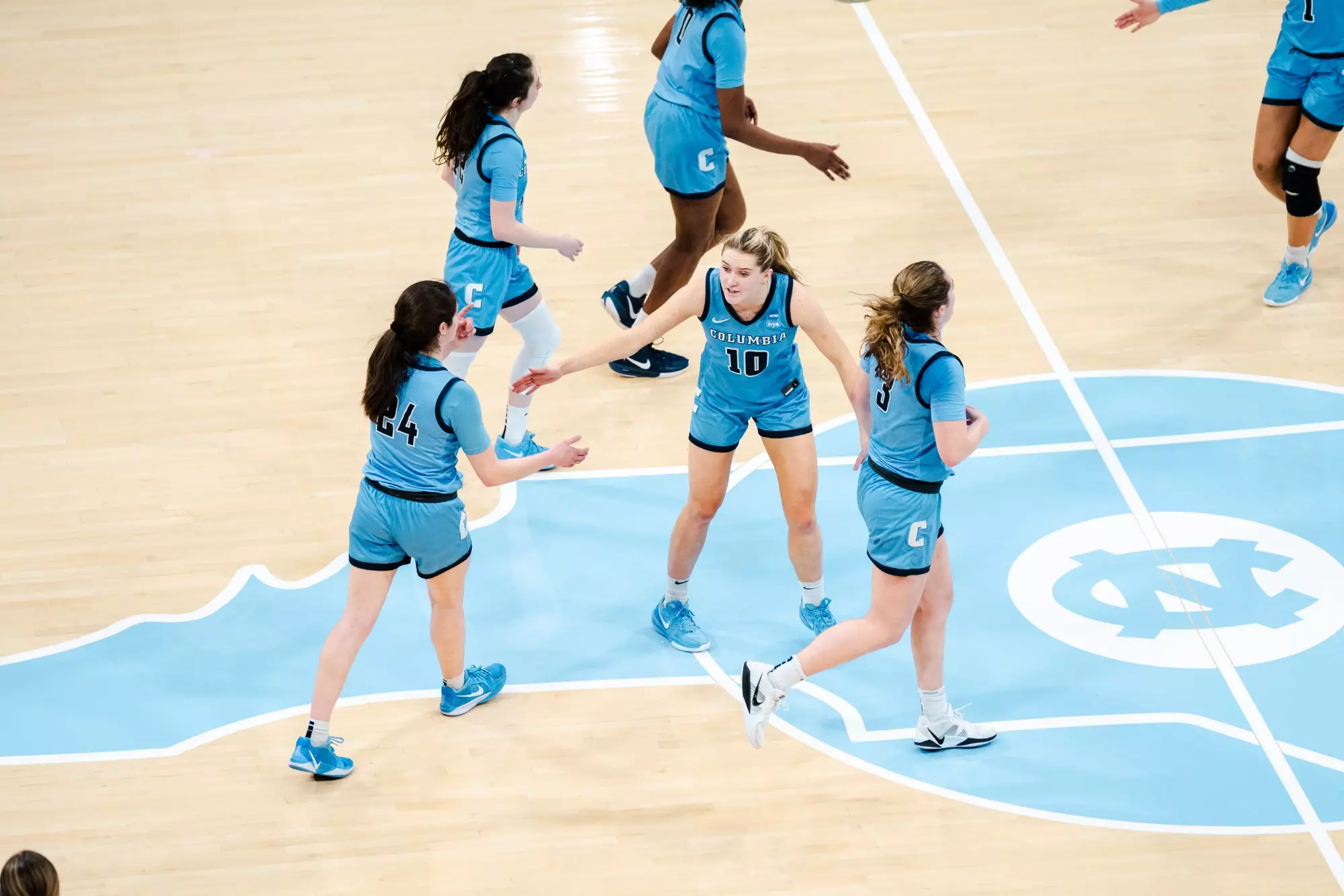 Columbia guard Kitty Henderson high-fives teammates Riley Weiss and Cecelia Collins near midcourt.