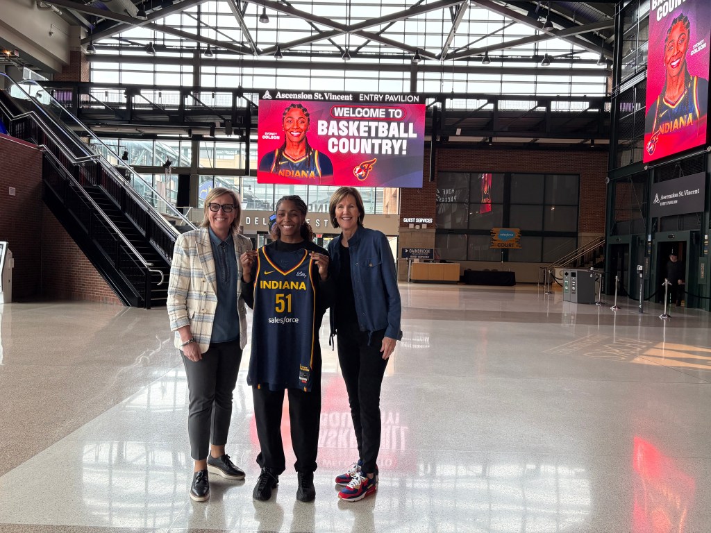 Indiana Fever guard Sydney Colson holds an Indiana Fever No. 51 jersey and smiles for a photo with general manager Amber Cox (left) and president of basketball operations Kelly Krauskopf.
