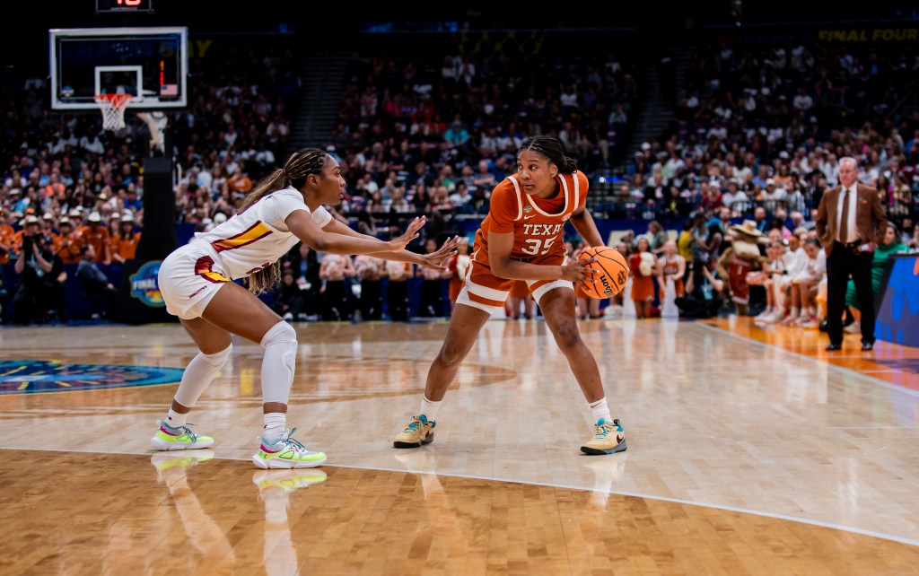Texas forward Madison Booker stands behind the 3-point line and holds the ball with two hands near her left knee as a South Carolina defender guards her tightly. Booker's eyes are up, assessing her options.