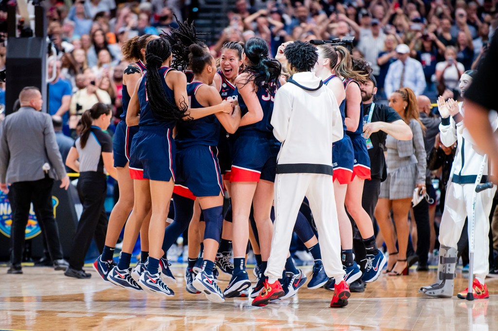 UConn players jump up and down in a huddle and scream after winning a national championship.