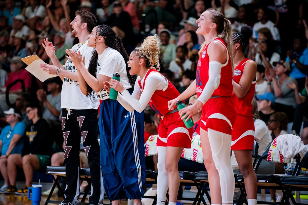 Team Lieberman guard Harmoni Turner stands on the sideline, leans forward, claps her hands and yells during an all-star game. The rest of the bench celebrates in similar fashion.