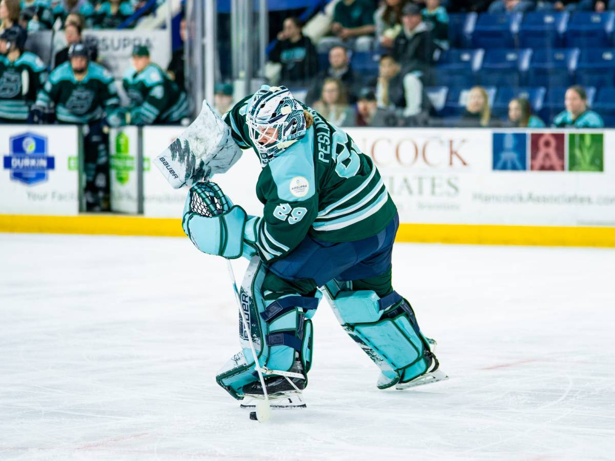 Peslarová is in between the faceoff circles, about to make a pass up-ice to her left. She is wearing a green home uniform.