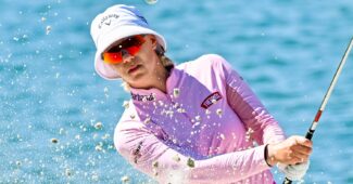 Madelene Sagstrom follows through on a bunker shot. The ball is popped up in the air and sand splashes up from the impact.