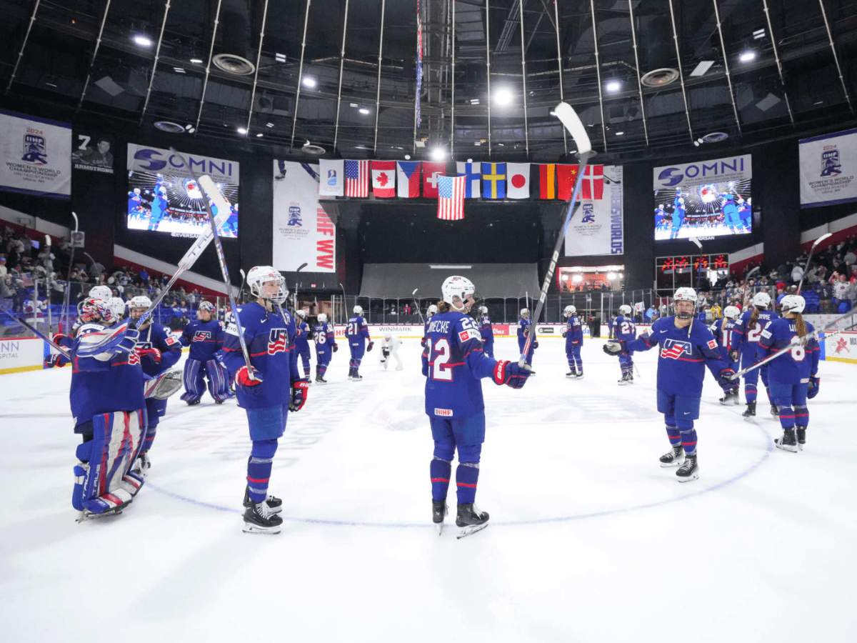 U.S. players raise their sticks in celebration at center ice. They are wearing blue uniforms.